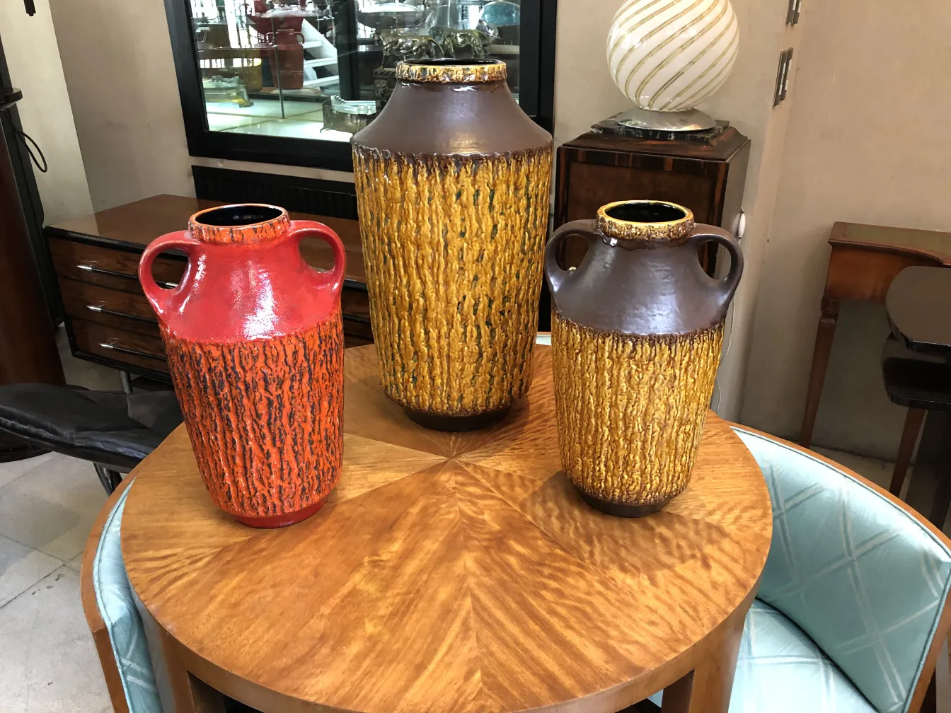 Trois vases anciens en céramique, un rouge, un jaune et un marron, sur une table en bois clair.