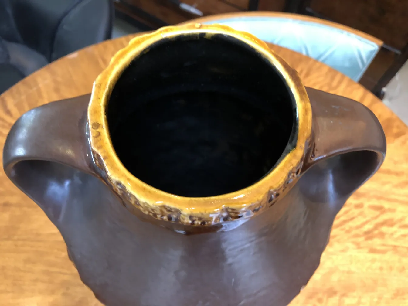暗い色と黄色の仕上げが施された古い陶器の花瓶が木製のテーブルの上にあります。