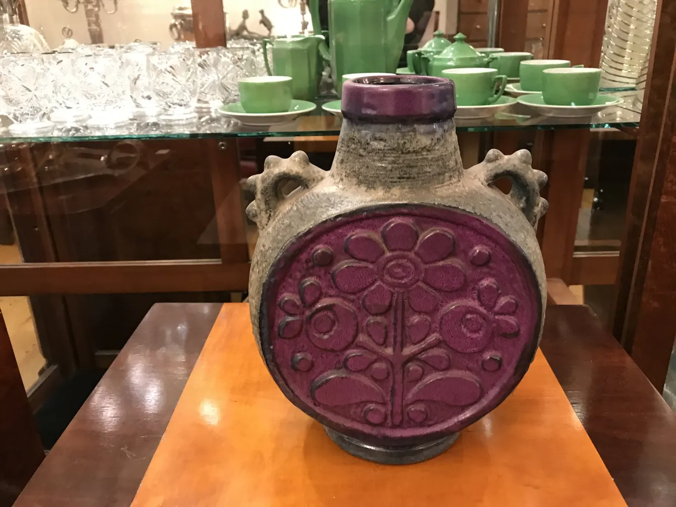 Antigua cerámica con diseño floral en colores vibrantes, decorativa y única, rodeada de cristalería y utensilios.