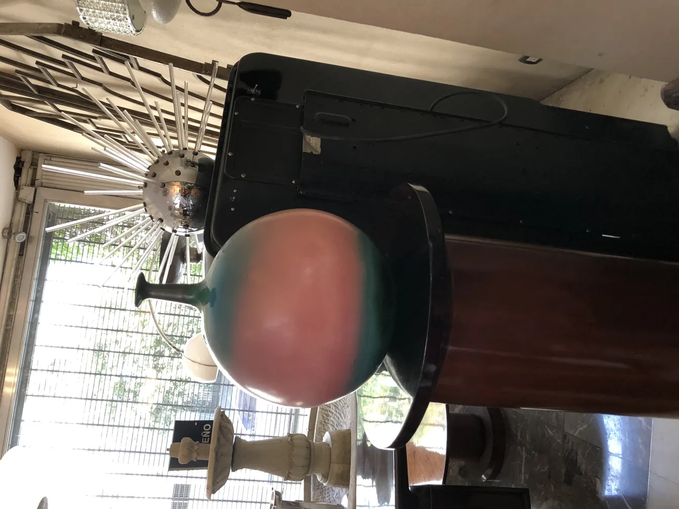 Esfera antigua de cerámica colorida con un acabado suave, en un ambiente poblado con otros objetos decorativos.