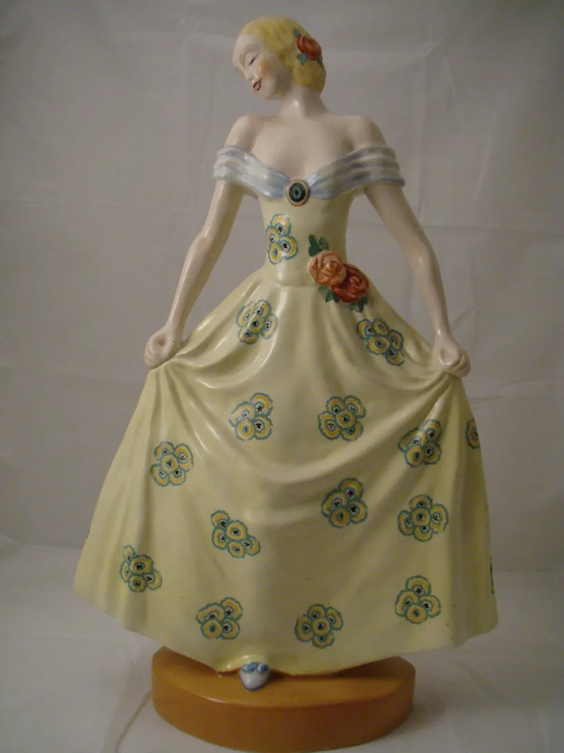 Antique Boch ceramic statue with painted female figure, yellow dress and floral patterns.