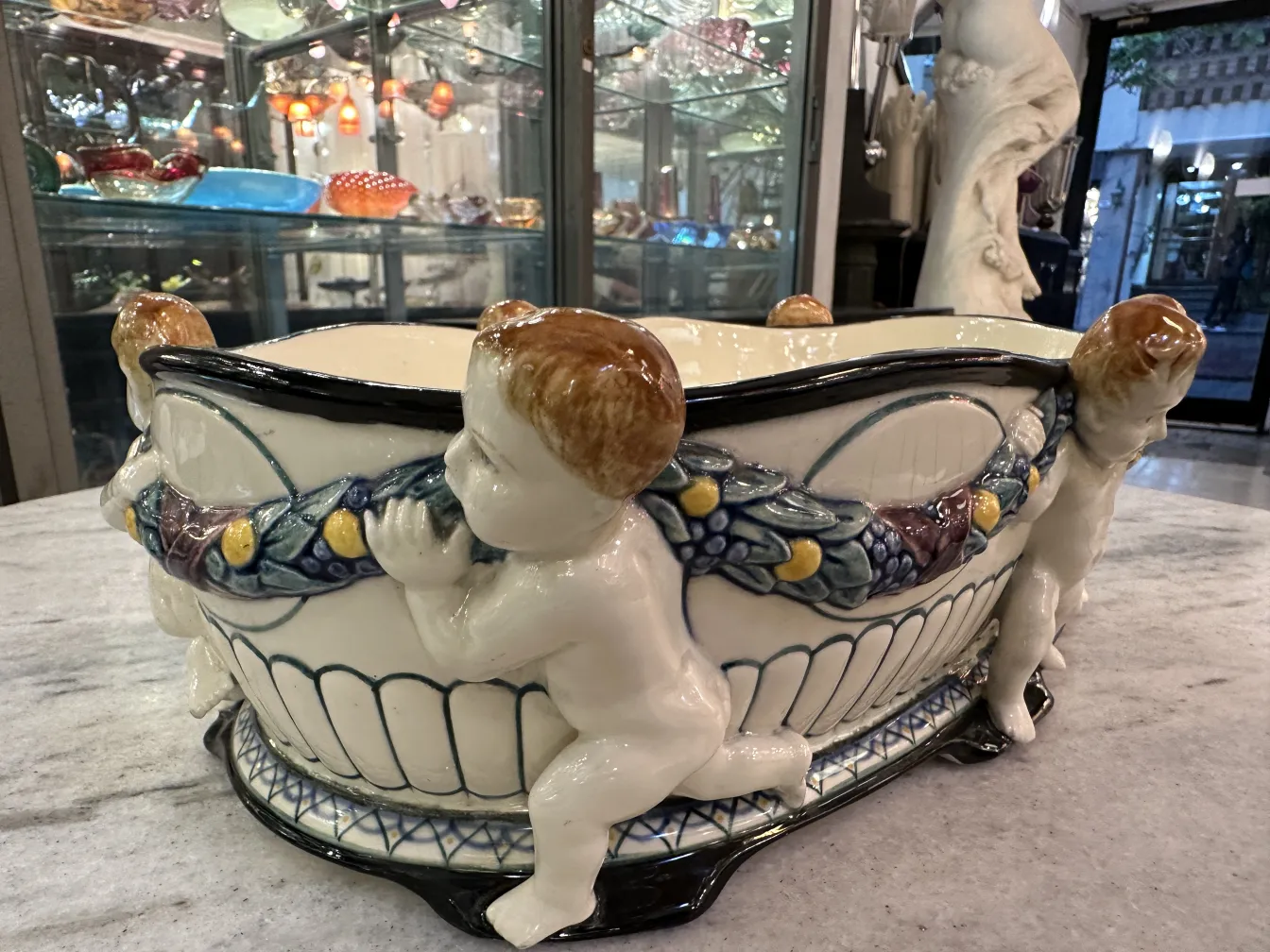 Antique ceramic featuring carved child figures, bright display background.