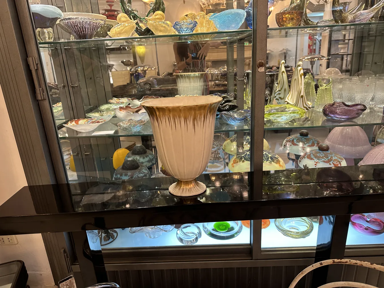 Vase en céramique ancienne avec des détails uniques et un design élégant, exposé dans une vitrine avec d'autres objets décoratifs.