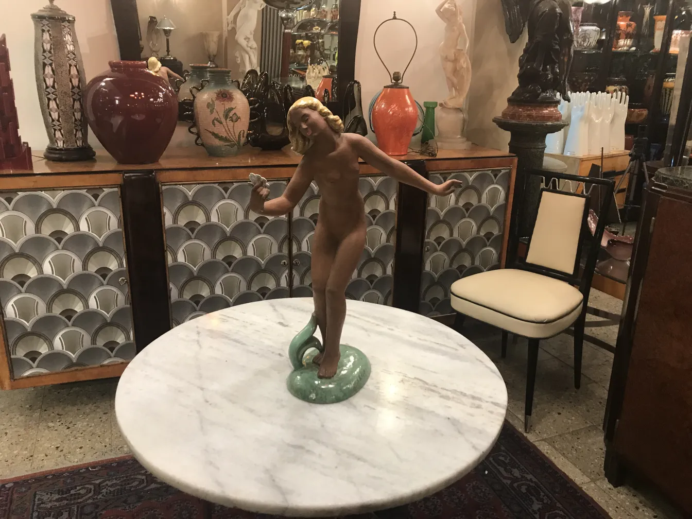 escultura antiga de cerâmica com figura feminina e serpente, fundo decorativo variado
