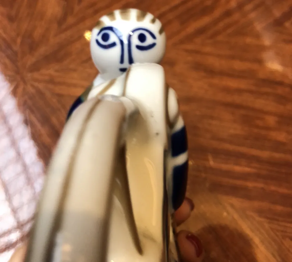 파란색 디테일과 표현력이 풍부한 얼굴이 있는 고대 장식 도자기 피규어, 반짝이는 나무 테이블 배경