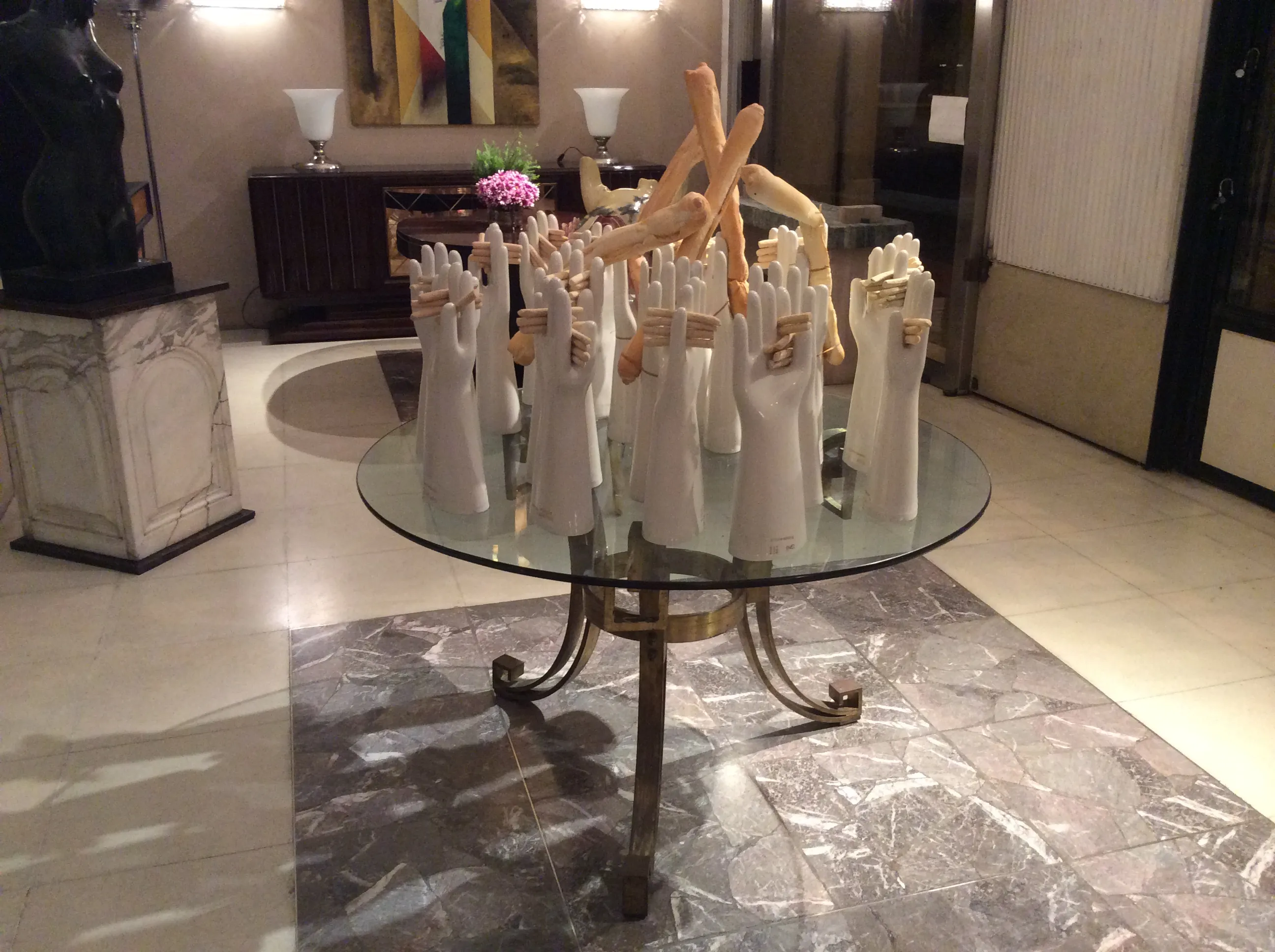 Mesa de comedor antigua para 4 personas con diseño Art Deco, decorada con manos escultóricas, en un ambiente elegante.