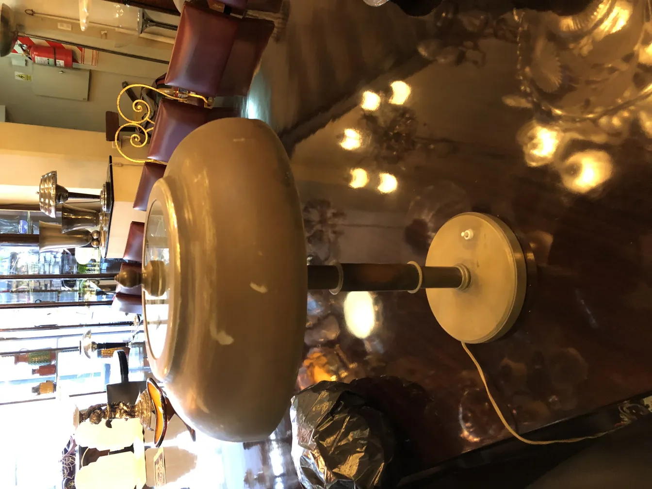 Lampe de bureau ancienne avec une base courbée et une lumière douce, entourée de chaises en cuir.