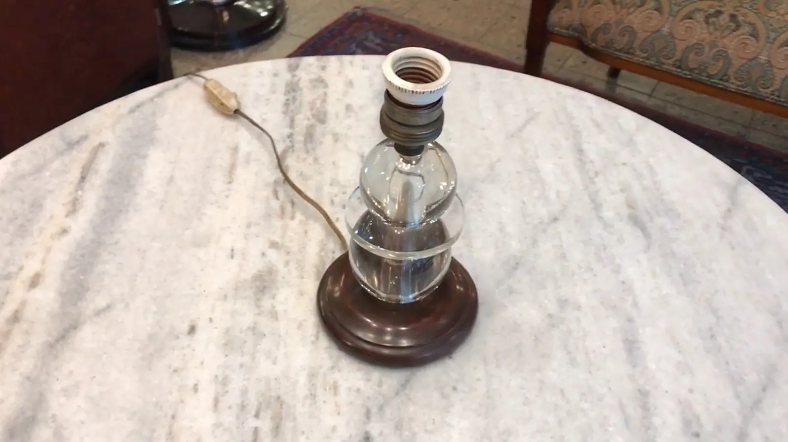 Vista dettagliata di una lampada da tavolo antica con base elegante e cavo visibile in un ambiente accogliente.