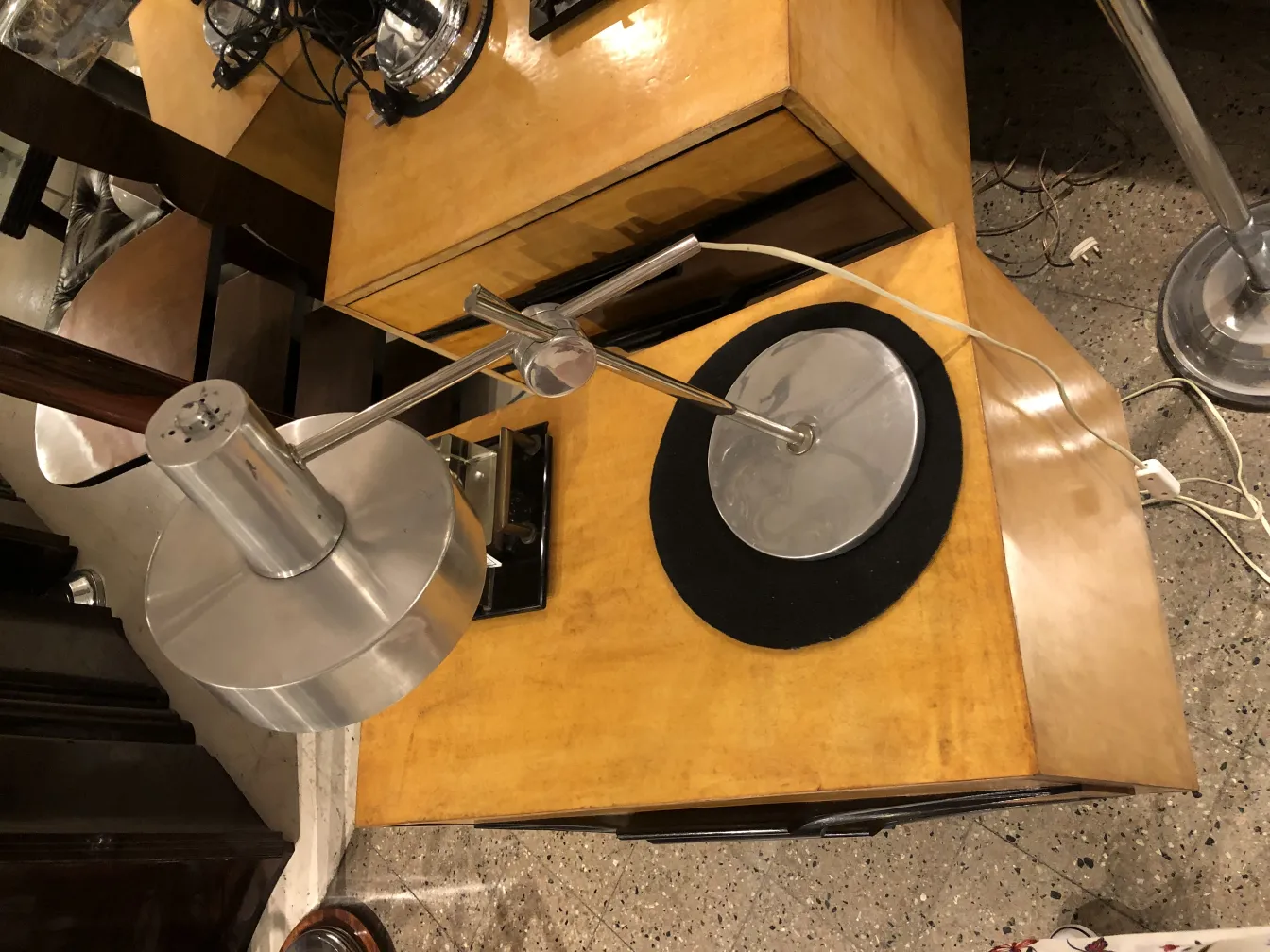 Lámpara de mesa antigua con base circular y diseño moderno. Fondo con mesa de madera clara.