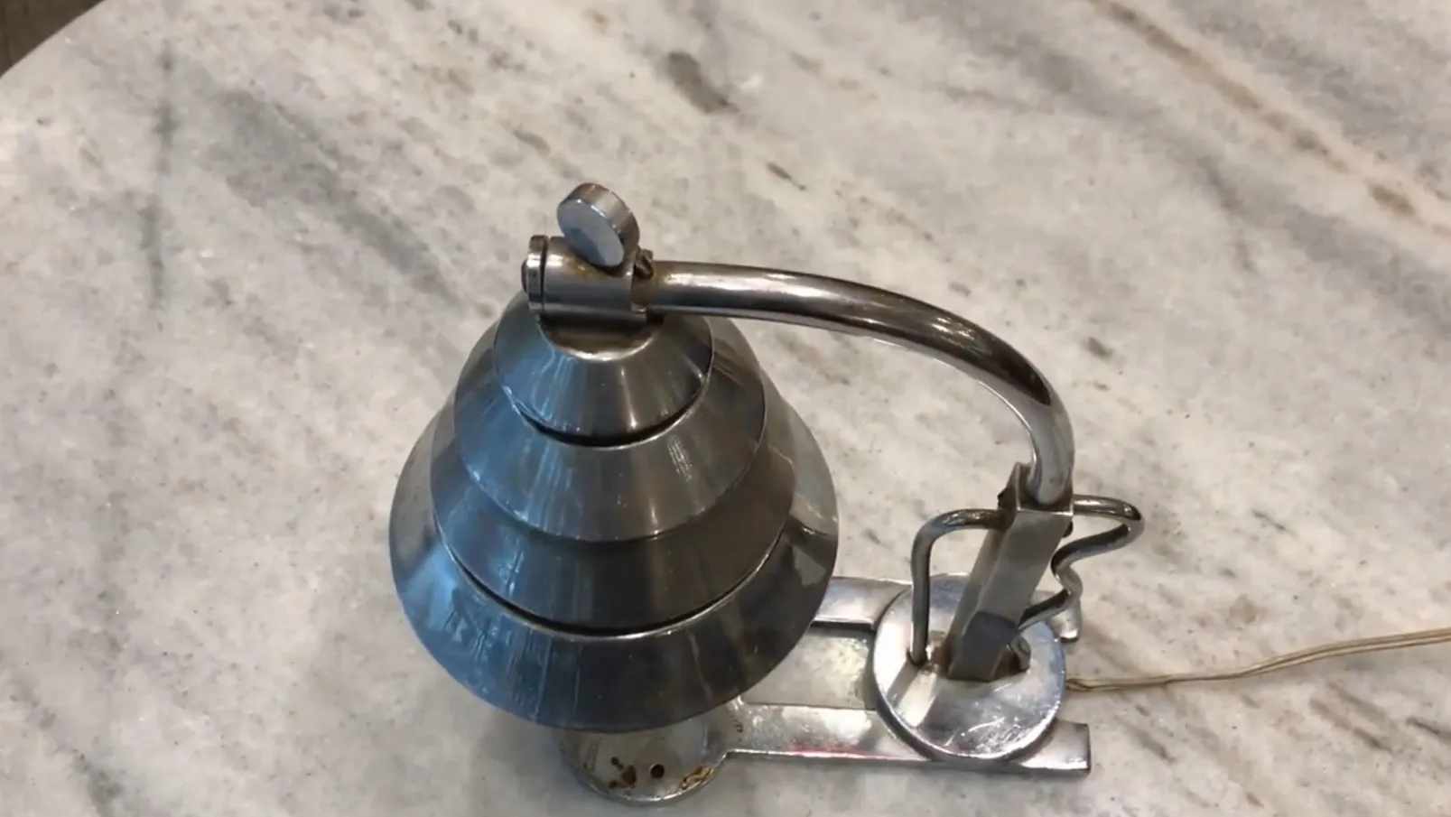 Lampe de bureau ancienne avec un design distinctif et élégant, tons métalliques brillants, sur une surface claire.