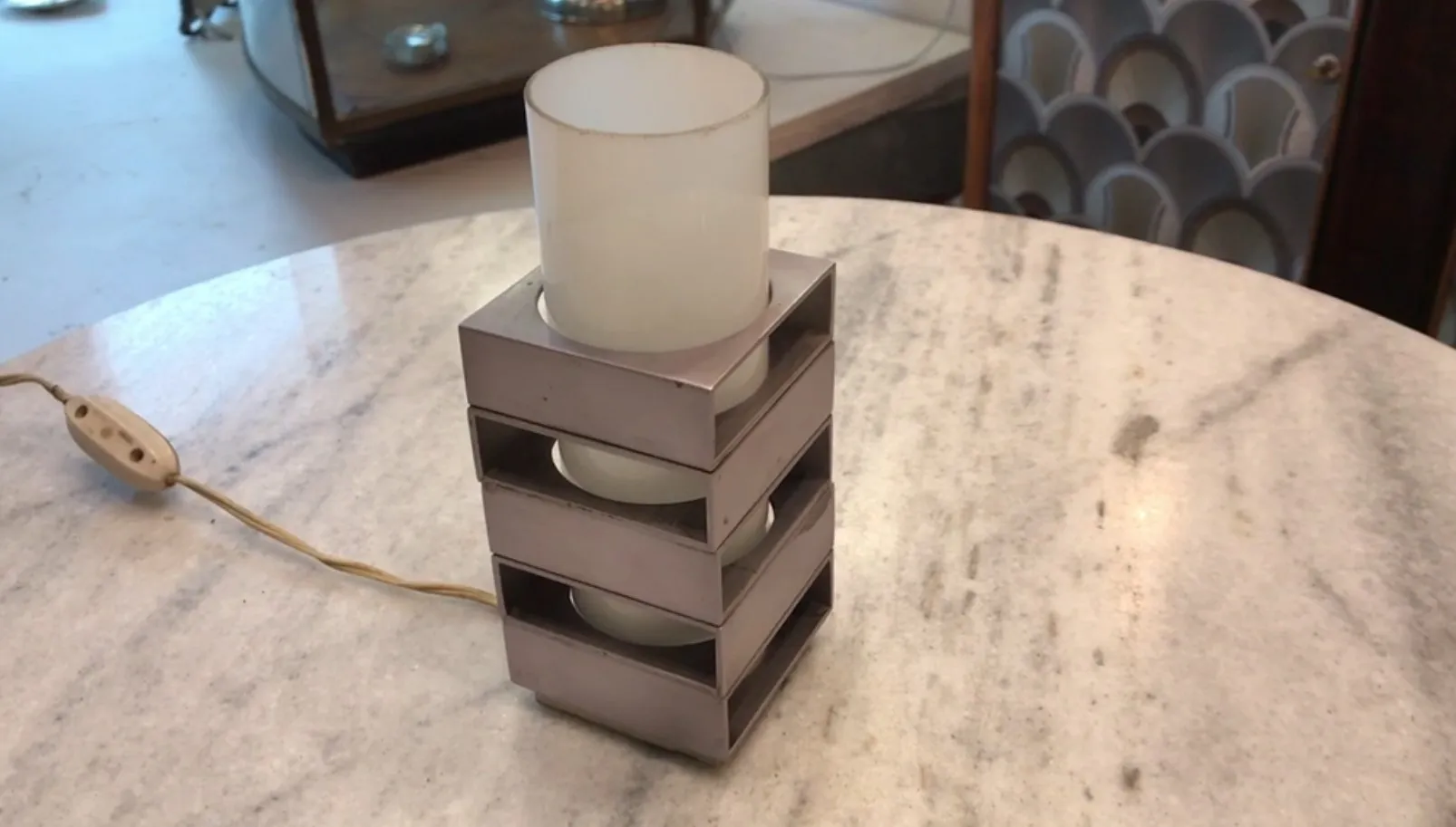 Lámpara de mesa antigua con base y pantalla de vidrio, en una mesa de mármol.