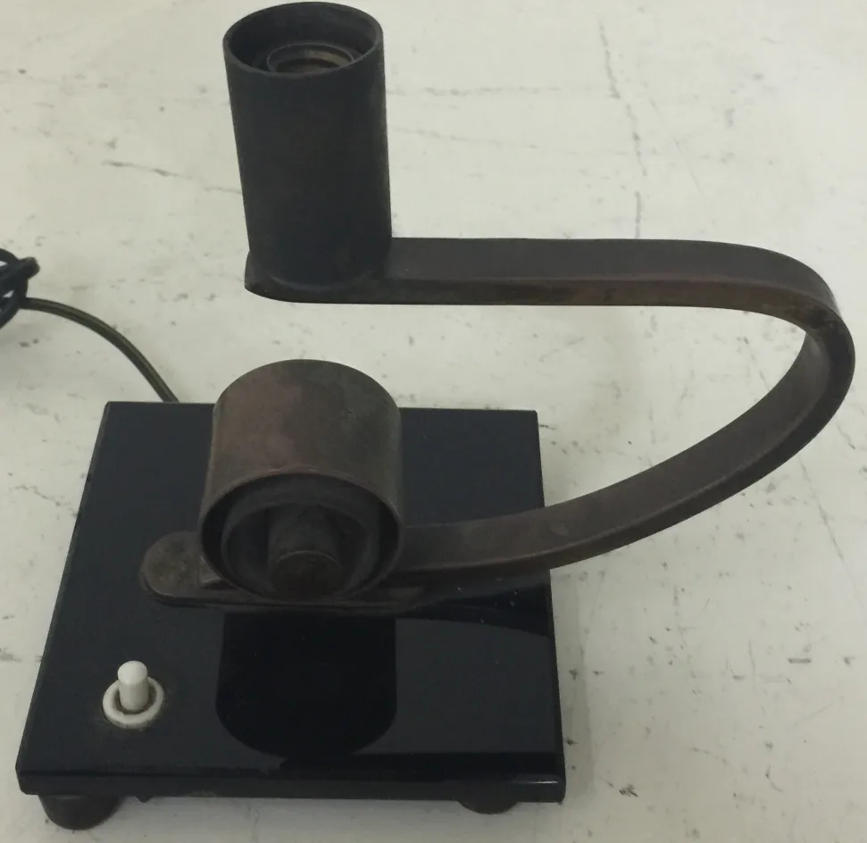 Lampada da tavolo antica con design moderno e base nera, ambientata in un contesto neutro.