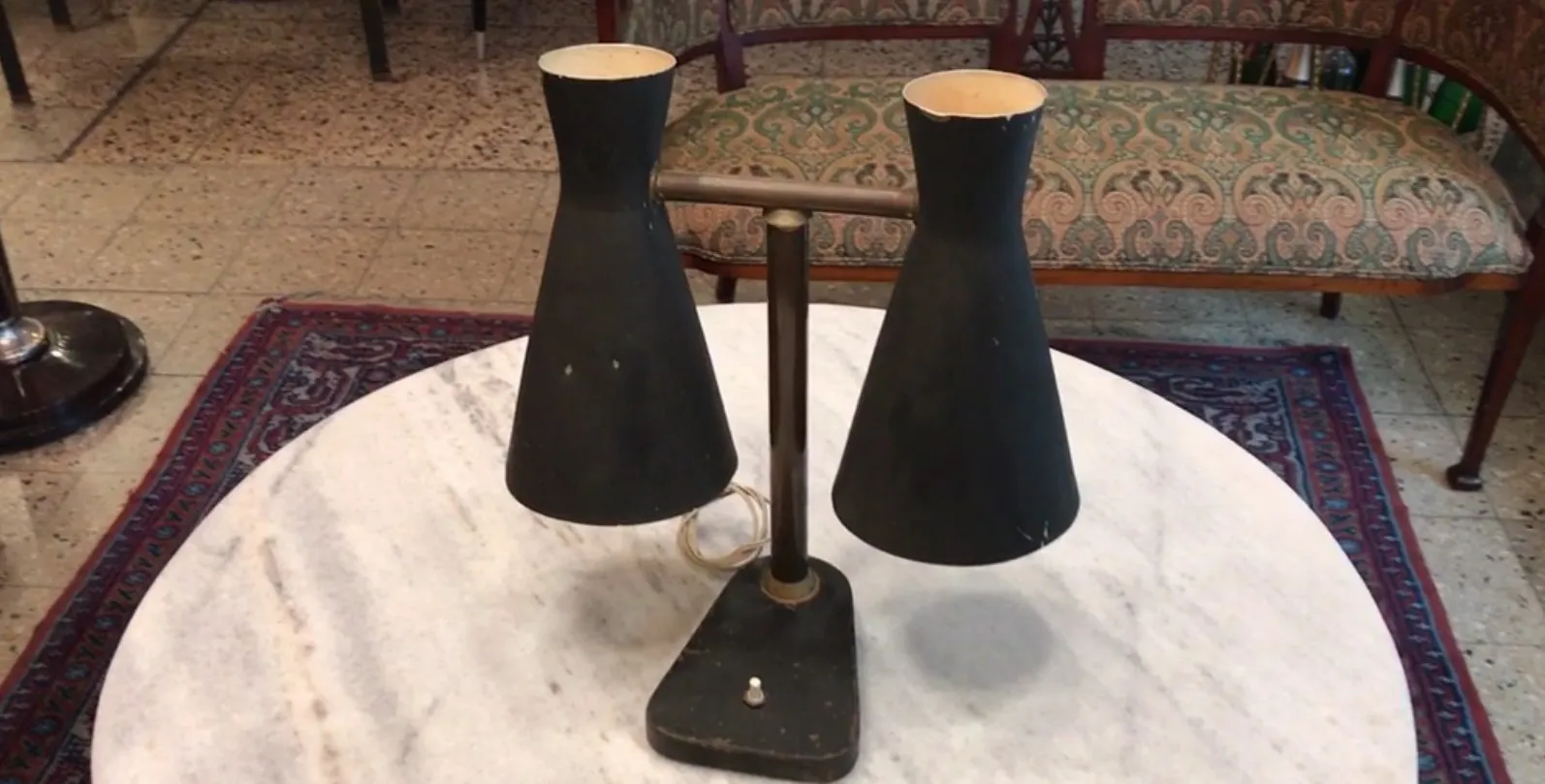 Luminária de mesa antiga de Serge Mouille com dois abajures em forma de cone sobre uma mesa de mármore.