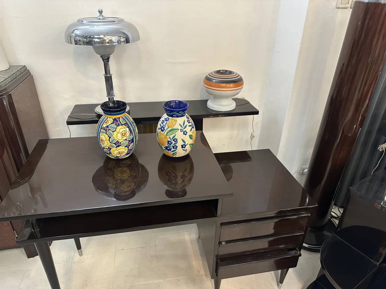 Lámpara de mesa antigua brillante sobre una mesa elegante con dos jarrones coloridos como fondo.