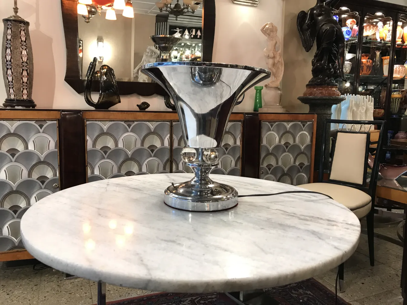 Lámpara de mesa antigua con base brillante en una mesa de mármol, rodeada de decoraciones.