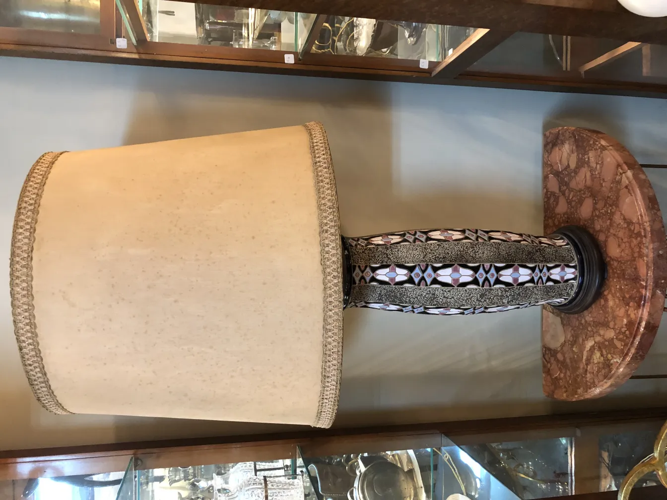 lámpara de mesa antigüa con tapa beis y base decorativa en tonos oscuros, en un entorno de antigüedades