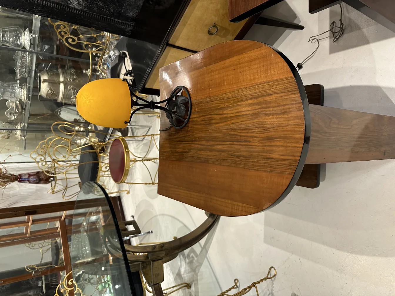 Antica lampada da tavolo con base nera e paralume giallo, in un ambiente di antiquariato.