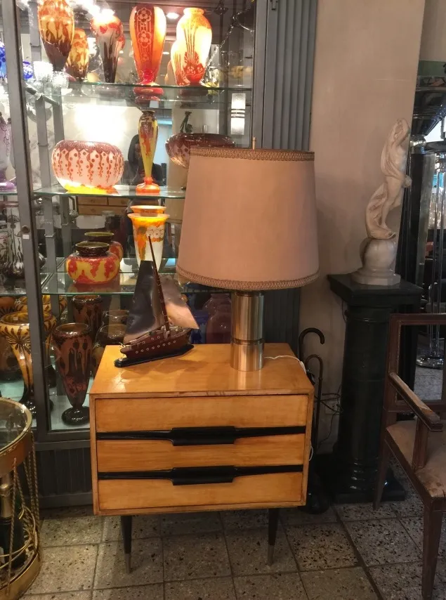 antique table lamp with beige shade on wooden furniture, surrounded by colorful decorations