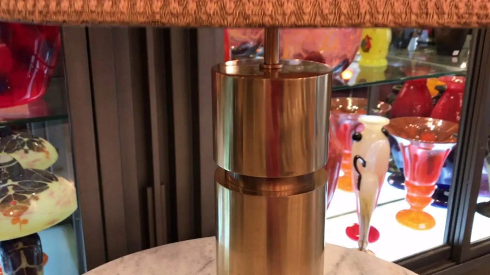 Lámpara de mesa antigua con sombra decorativa, rodeada de objetos coloridos.