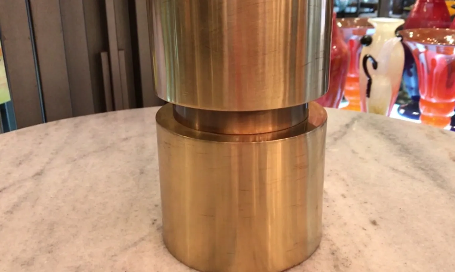 luminária de mesa antiga com formato cilíndrico, tons dourados, em uma mesa de mármore