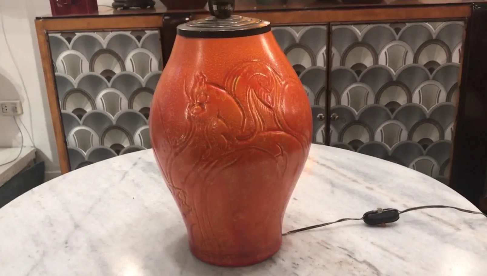 Lámpara de mesa antigua de forma ovalada y color naranja, decorada con motivos ornamentales, ambiente elegante.