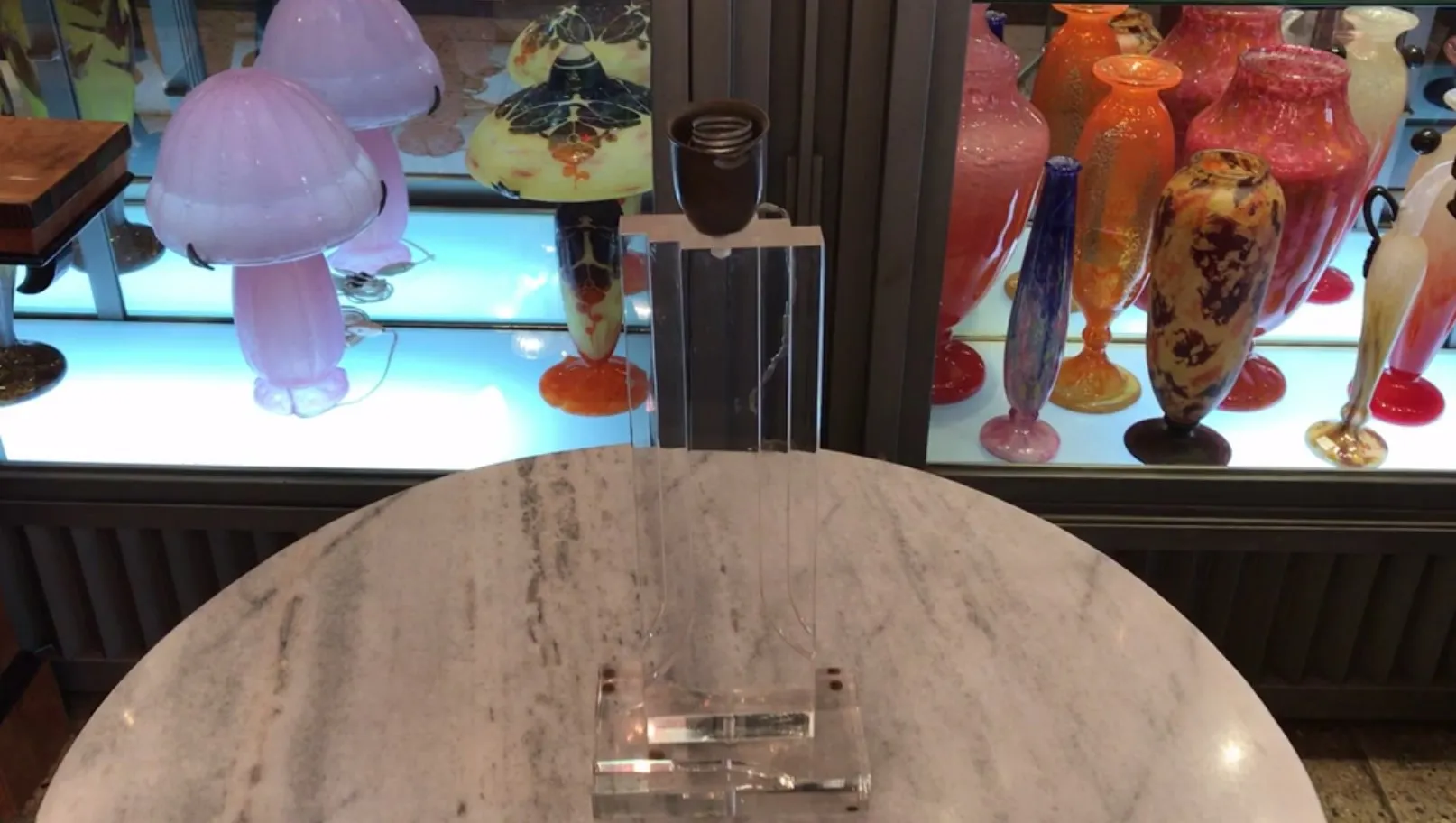 lampe de bureau rose antique avec base en verre, illuminant des assiettes décoratives colorées en arrière-plan