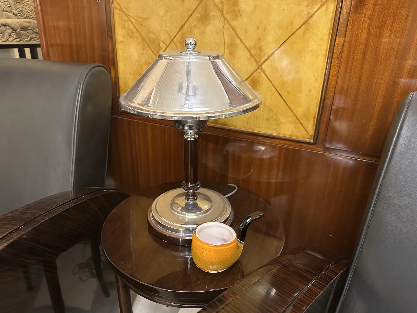 Luminária de mesa antiga de design clássico em um ambiente elegante, ao lado de uma xícara decorativa.