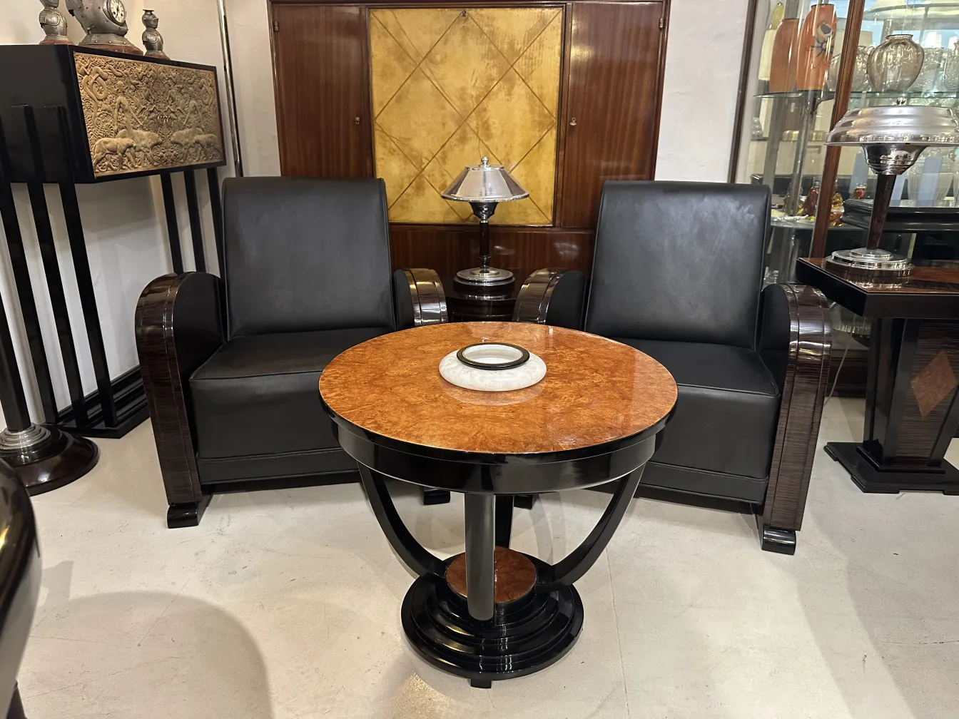 Lampada da tavolo antica accesa in un ambiente elegante, con poltrone nere e un tavolo in marmo, evidenziando il suo design classico.