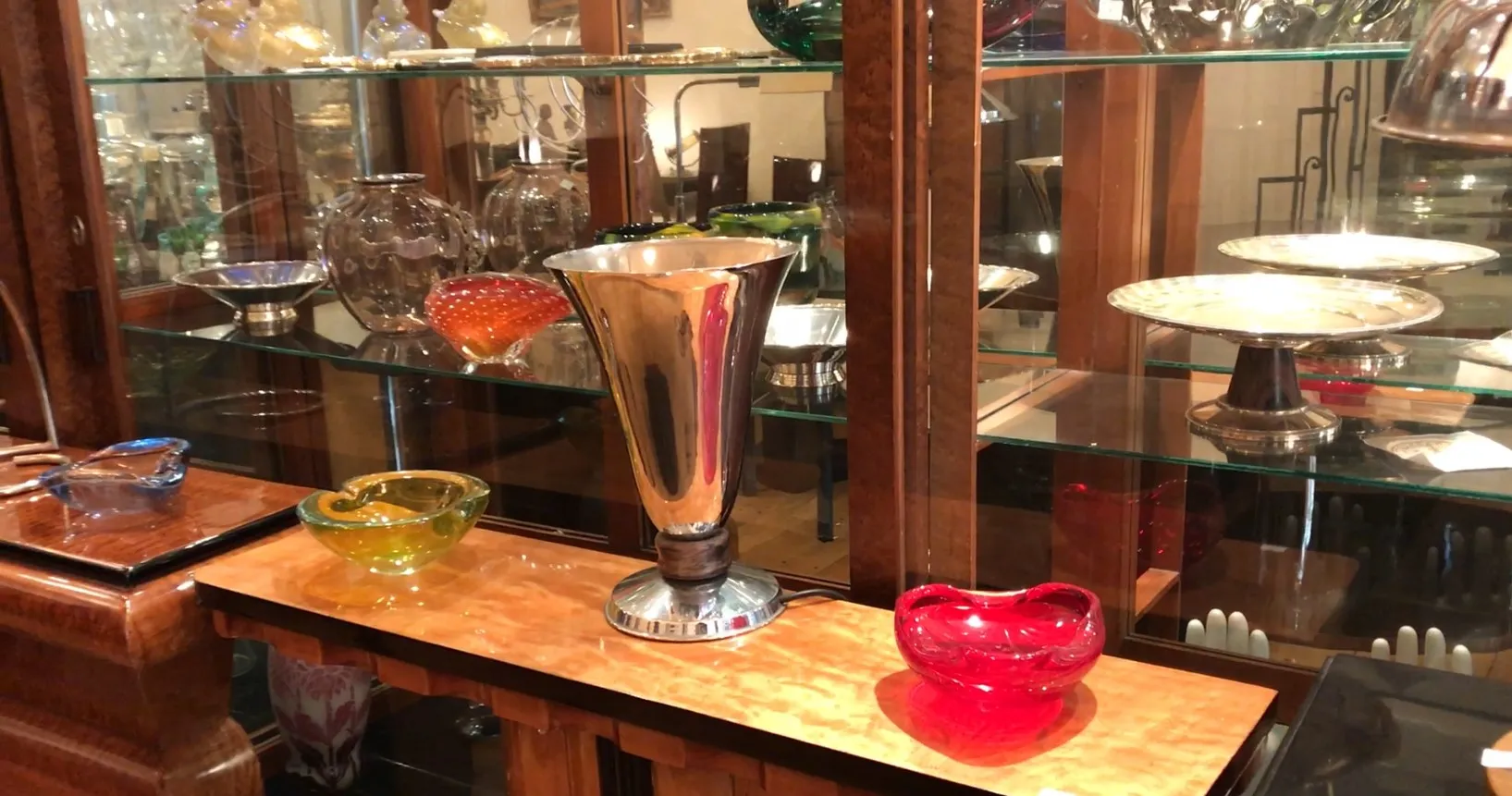 Lampada da tavolo antica con design luminoso, circondata da oggetti in vetro in un ambiente elegante.