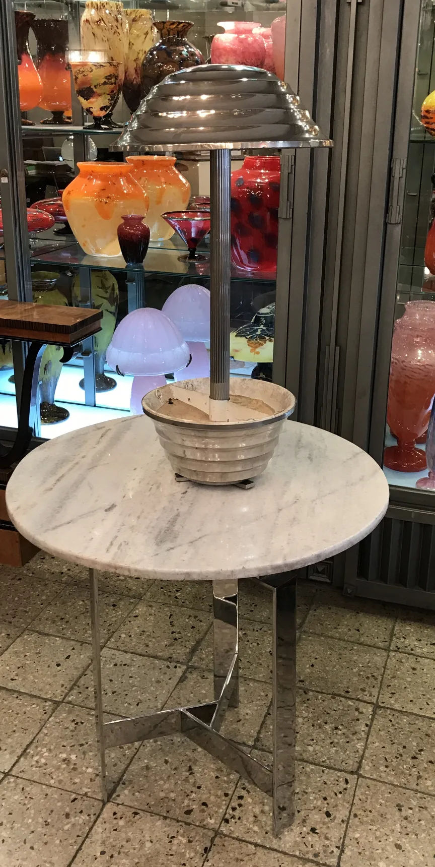 Lámpara de mesa antigua con base de diseño tallado, rodeada de coloridas piezas de vidrio.