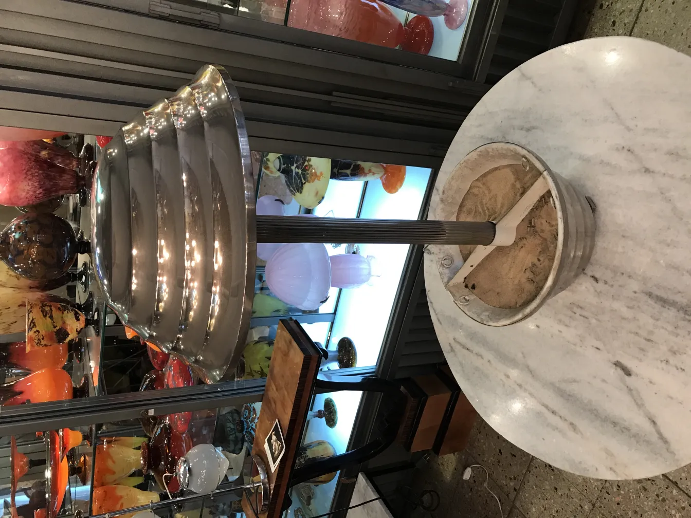 Antigua lámpara de mesa con base redonda en ambiente de antigüedades, rodeada de otros objetos decorativos.