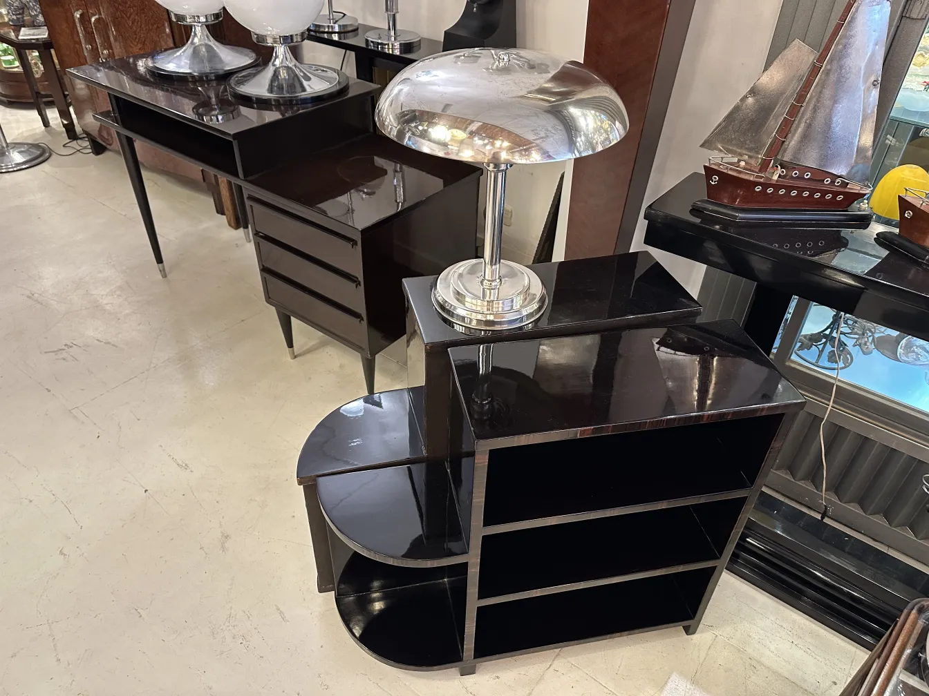 Lámpara de mesa antigua con base metálica brillante, sobre un mueble oscuro.