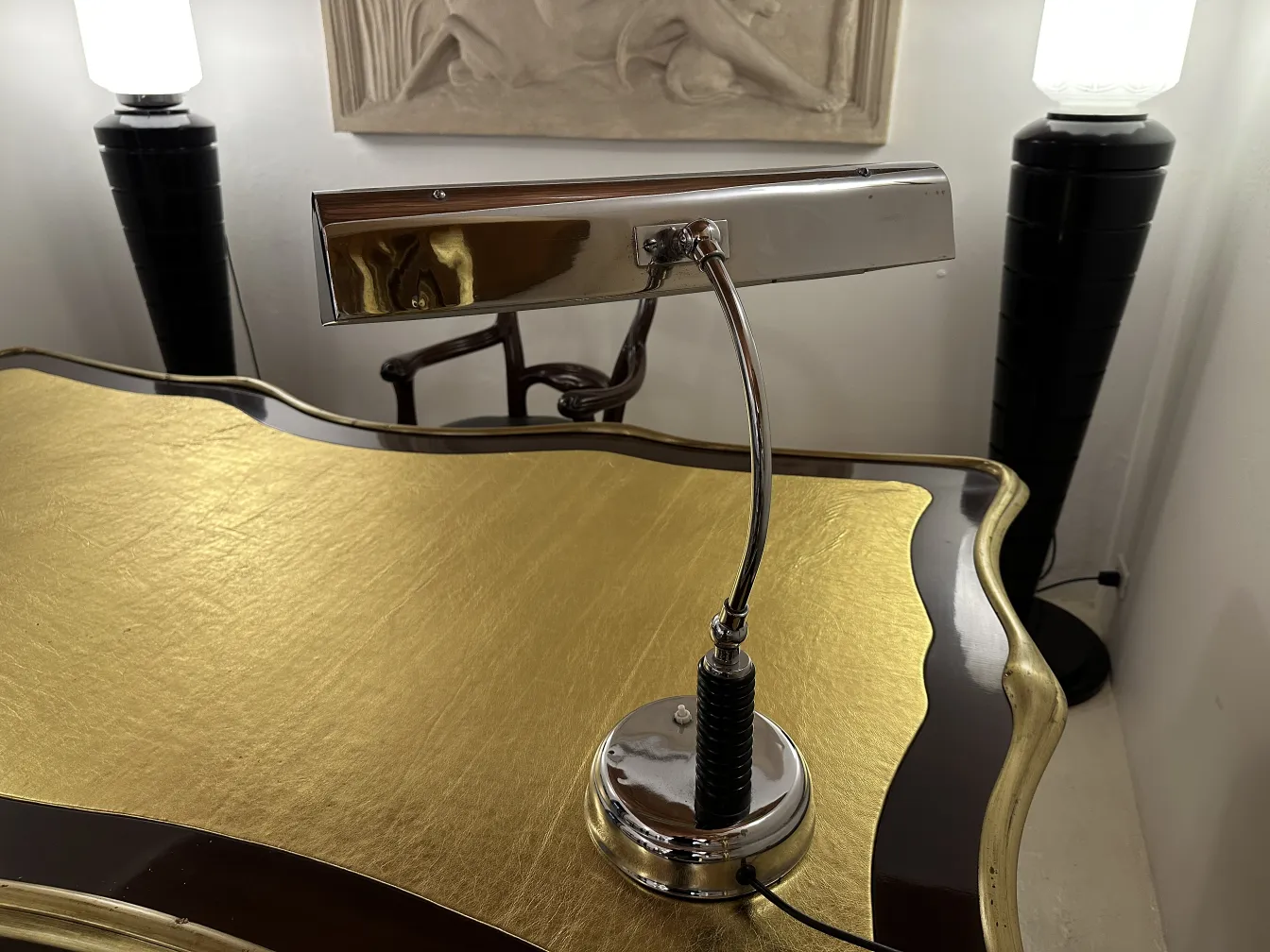 Luminária de mesa antiga com base brilhante em uma mesa dourada, cercada por outros elementos de decoração.