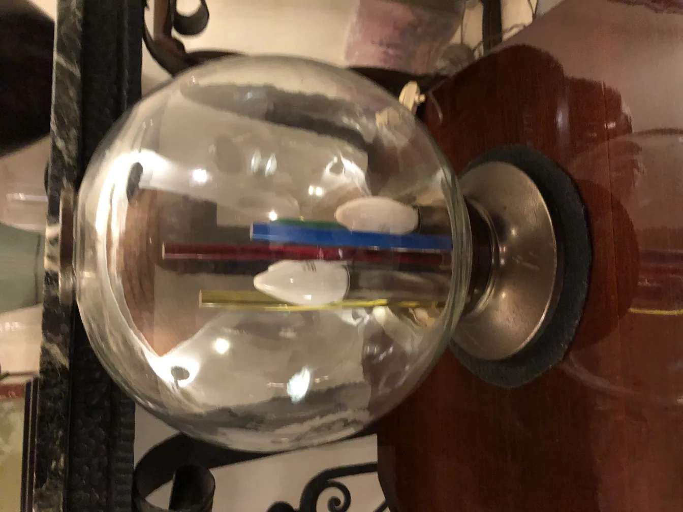 Lámpara de mesa antigua con globo y tubos de colores sobre mesa de madera.