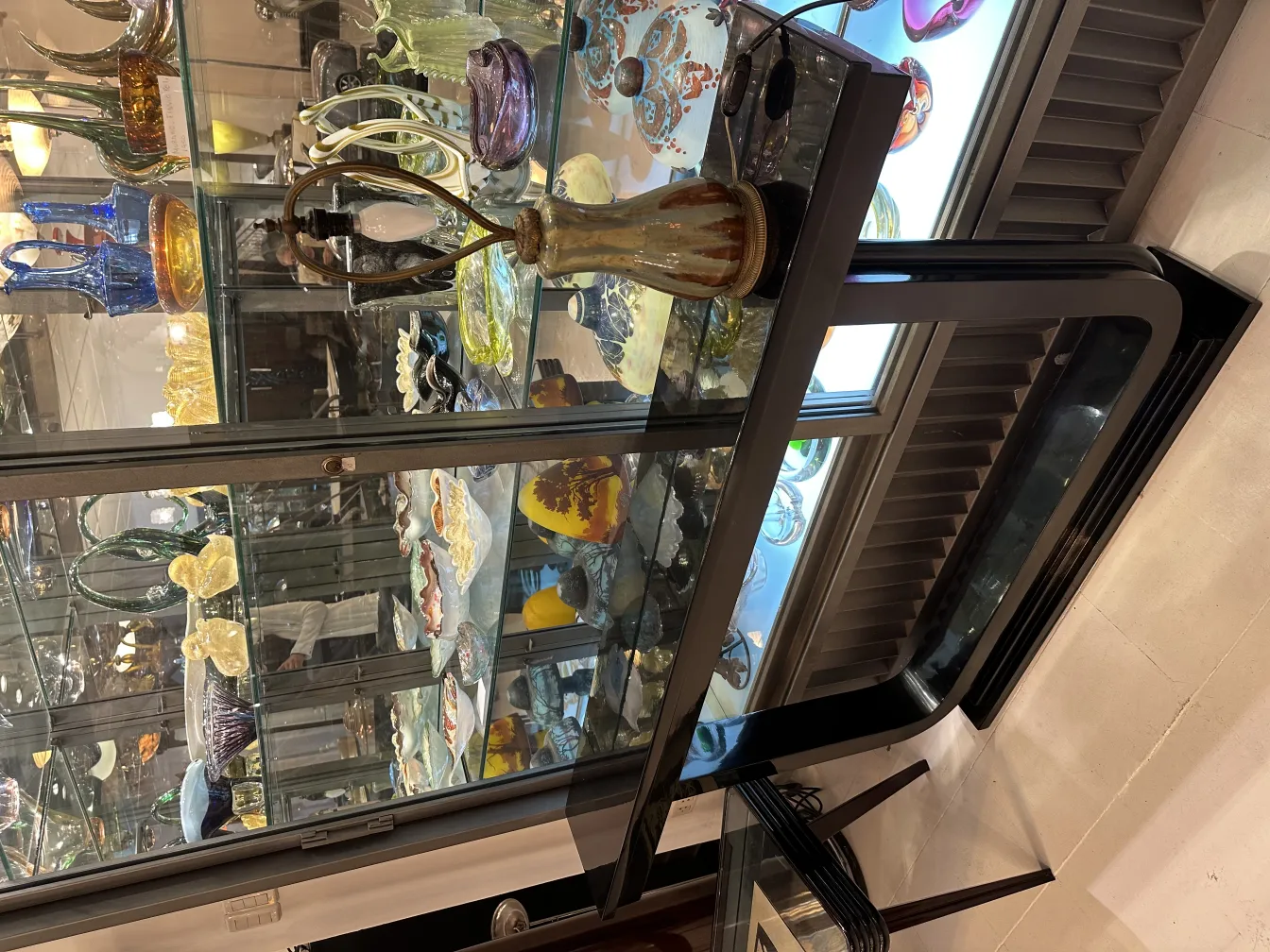 Antique decorative table lamp with elegant design and warm light, surrounded by art in display case.