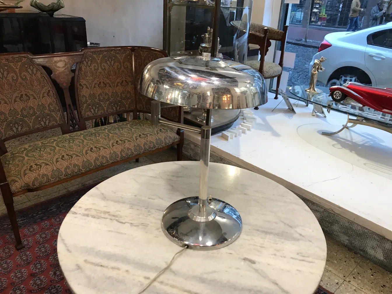 Lámpara de mesa antigua con base redonda y luz suave, en un ambiente acogedor con un sofá. Ideal para decoración.