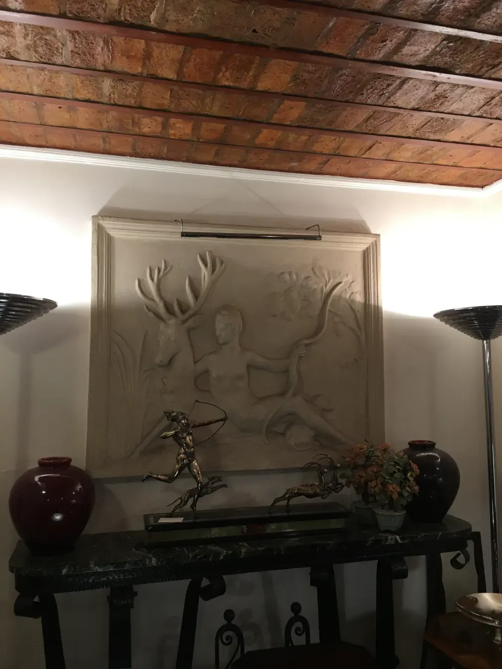 Antique decorative console with figures, flowers, and red vase.