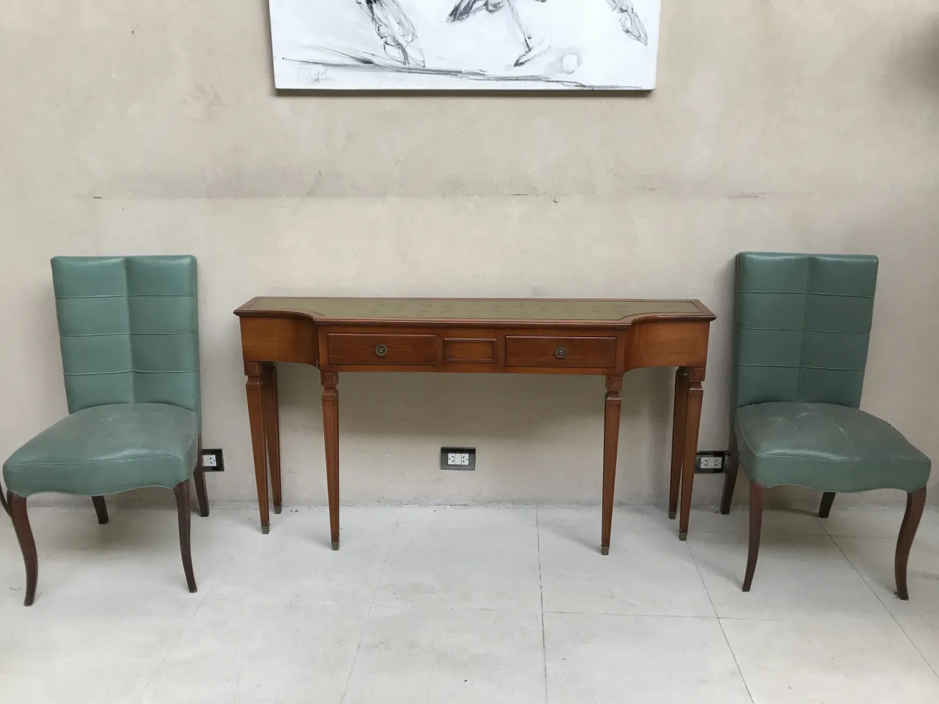 Antique console with two drawers and green chairs beside it.