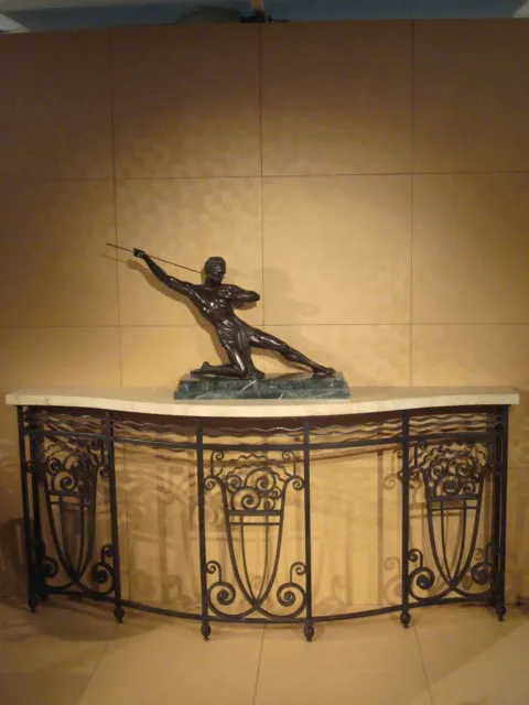 Consola antigua con escultura sobre la parte superior, rodeada de un fondo simple.