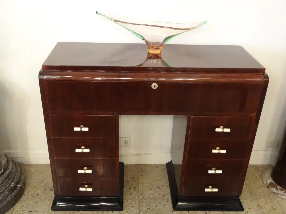 Consola antigua con varios cajones y decoración superior.