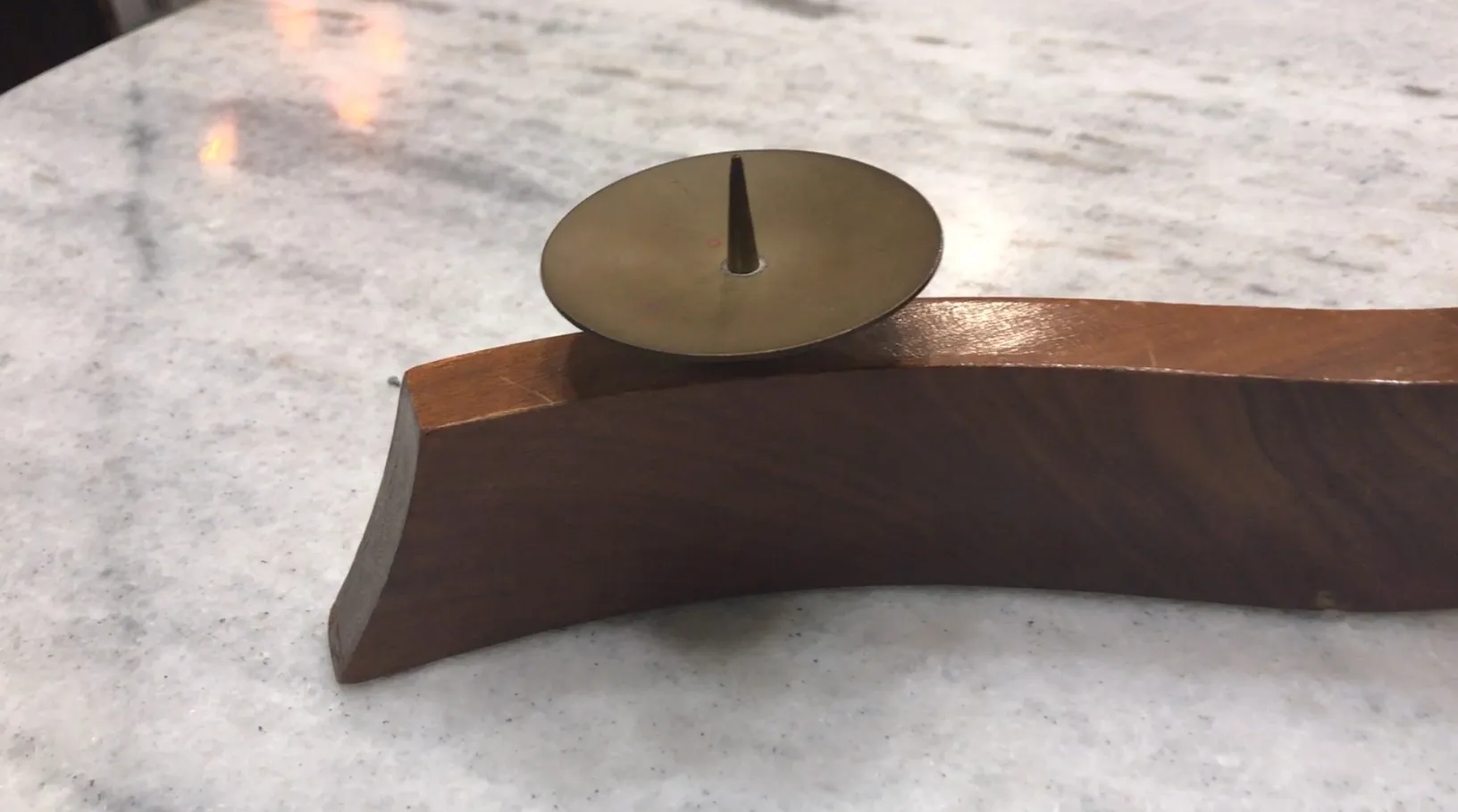 Castiçal antigo com base curva e detalhe simples no centro sobre uma mesa de mármore.