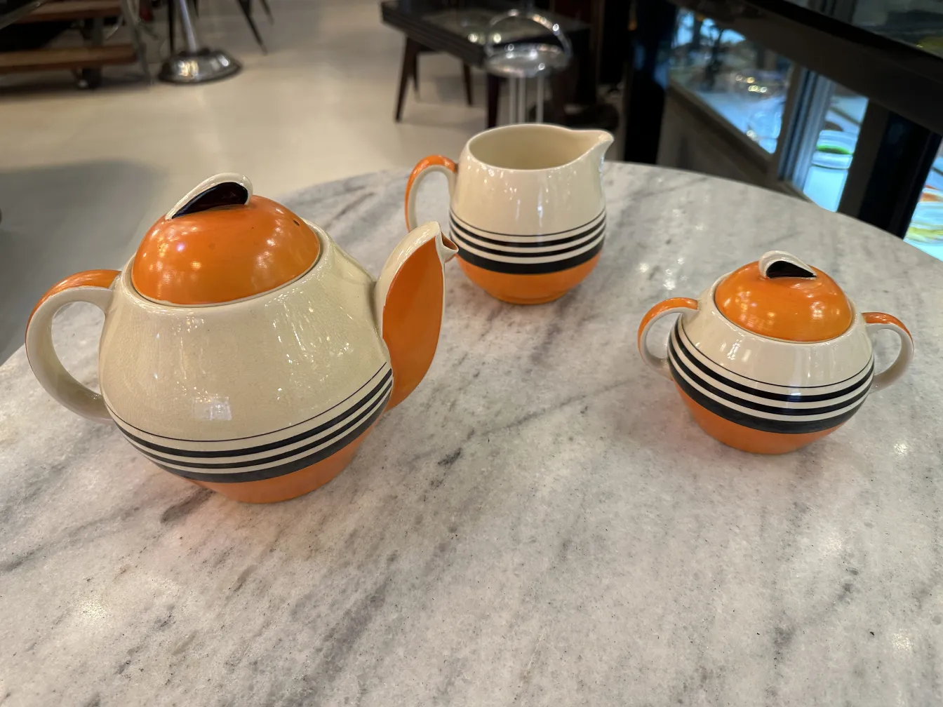 Conjunto de chá antigo em tons de laranja e bege, com detalhes em preto. Inclui bule e creme.