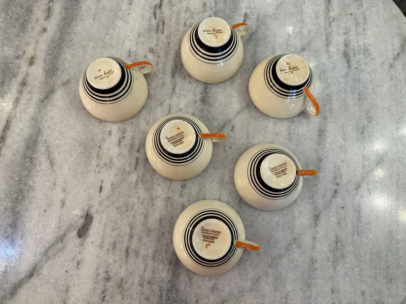 Antiguo juego de té con seis tazas de cerámica decoradas con rayas negras y naranjas sobre una mesa de mármol.