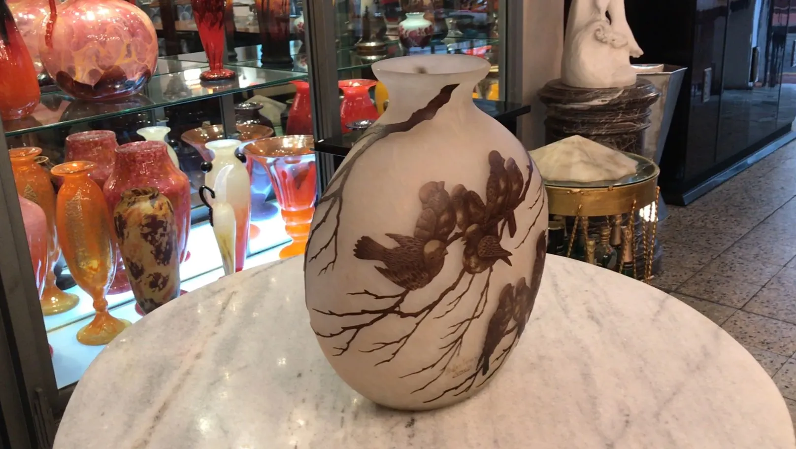 Verre signé avec motif d'oiseaux exposé parmi des vases colorés.