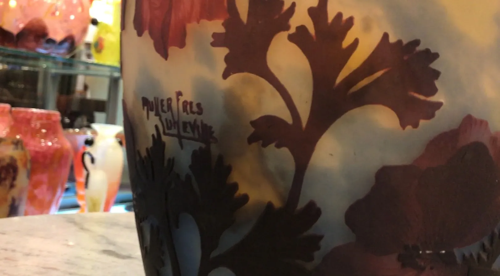 Vetro firmato Muller Freres con motivo floreale in toni caldi, sfondo sfocato.