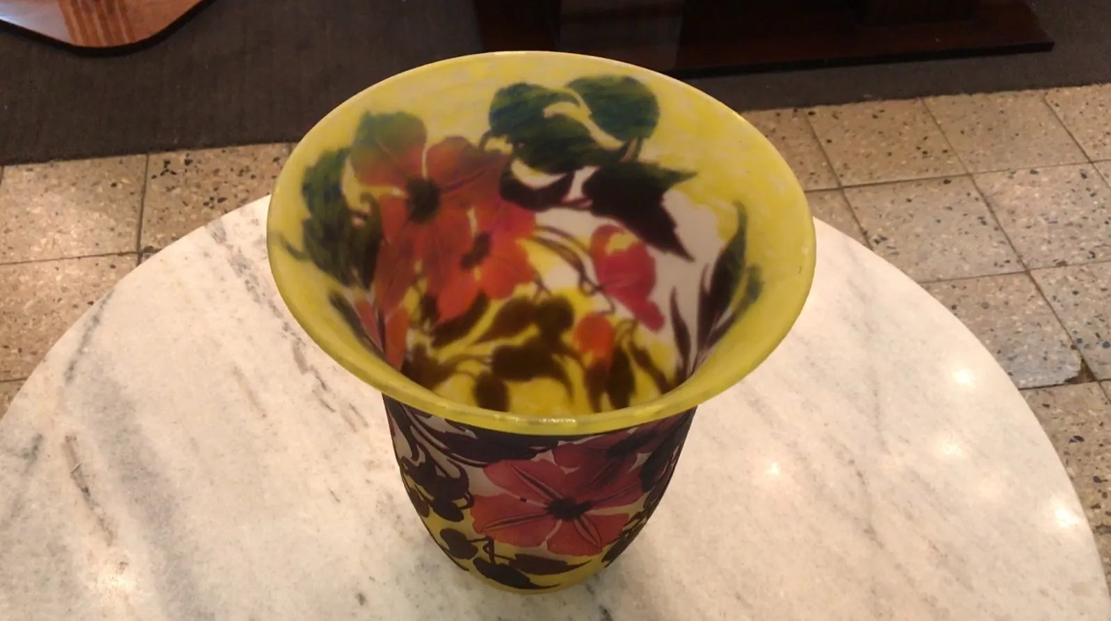 Vaso antigo de vidro assinado Muller Fres com design de flores coloridas contra um fundo claro, ambientado em uma mesa de mármore.