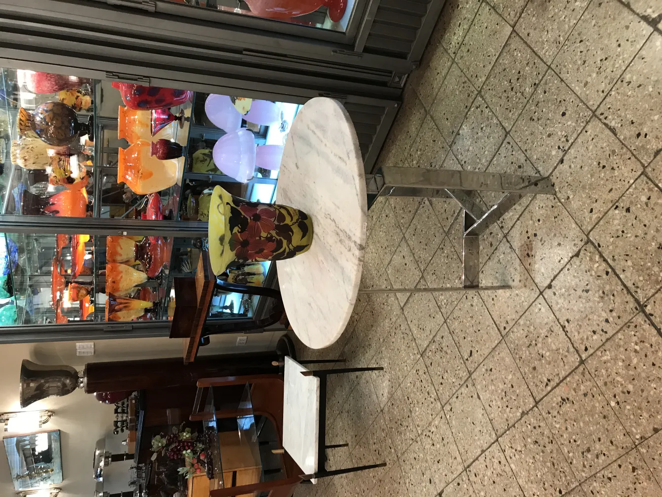 Antikes Glas mit der Unterschrift Muller Fres, mit verschiedenen Farben und ästhetischen Formen, umgeben von dekorativen Objekten.