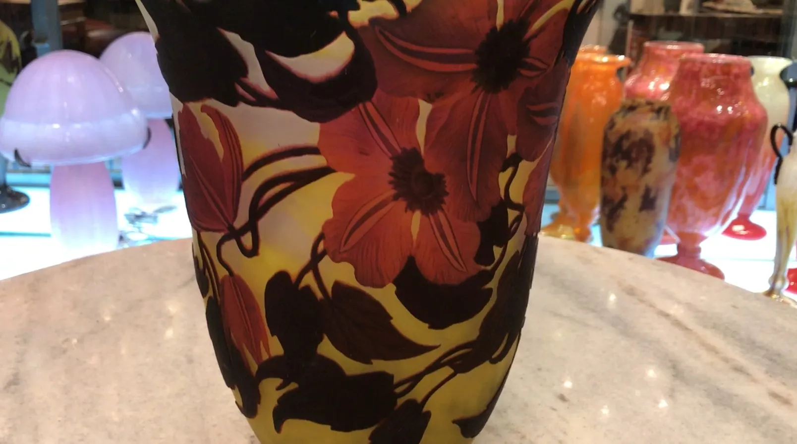 Vidrio firmado Muller Freres con motivo de flores en tonos cálidos, rodeado de otros objetos decorativos.