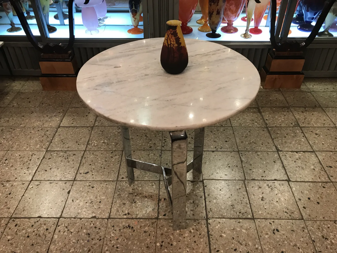 Vidro assinado muller fres em uma mesa antiga, com objetos decorativos ao fundo.