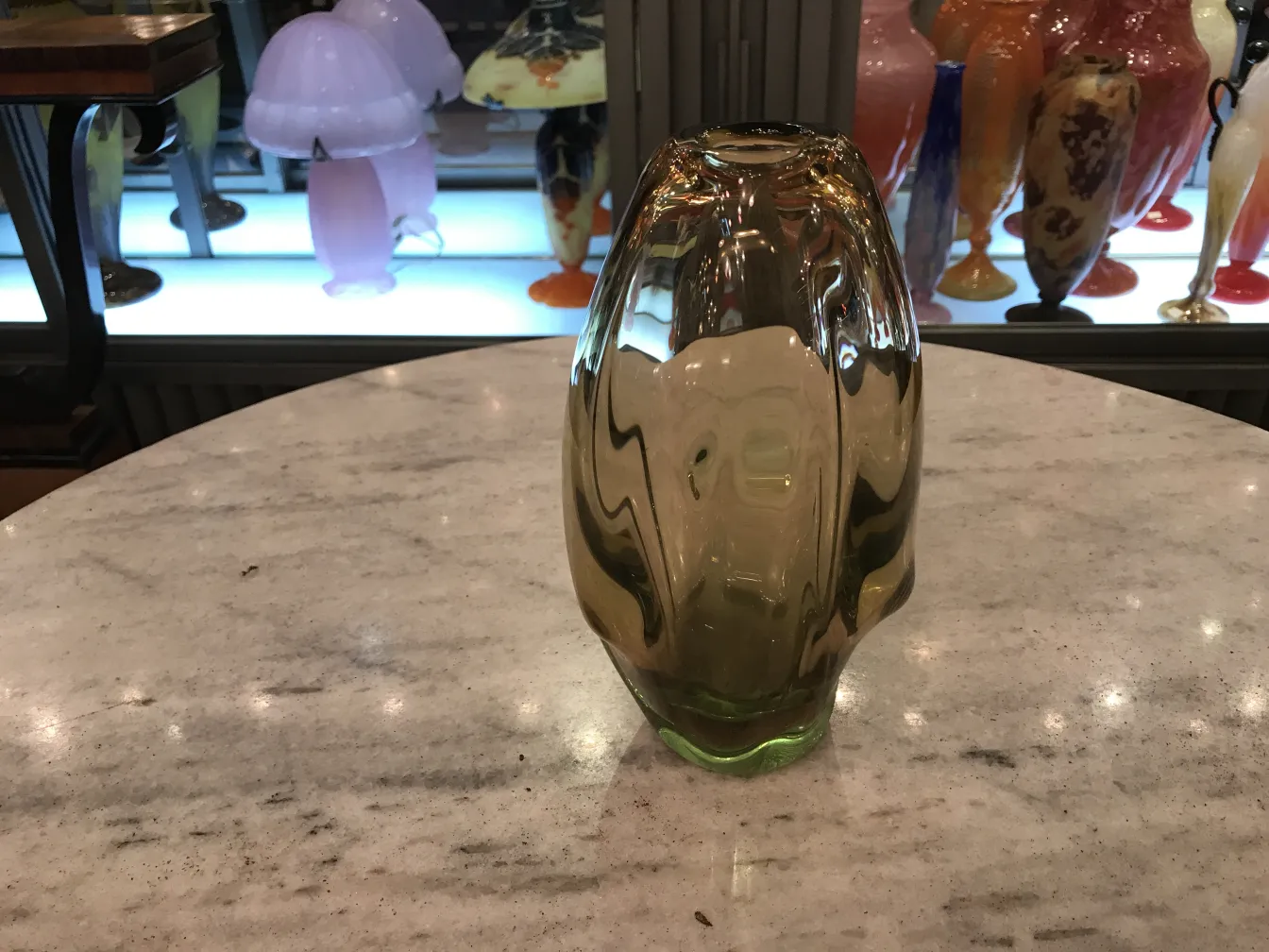 vaso di murano antico di colore chiaro su un tavolo con oggetti decorativi sullo sfondo